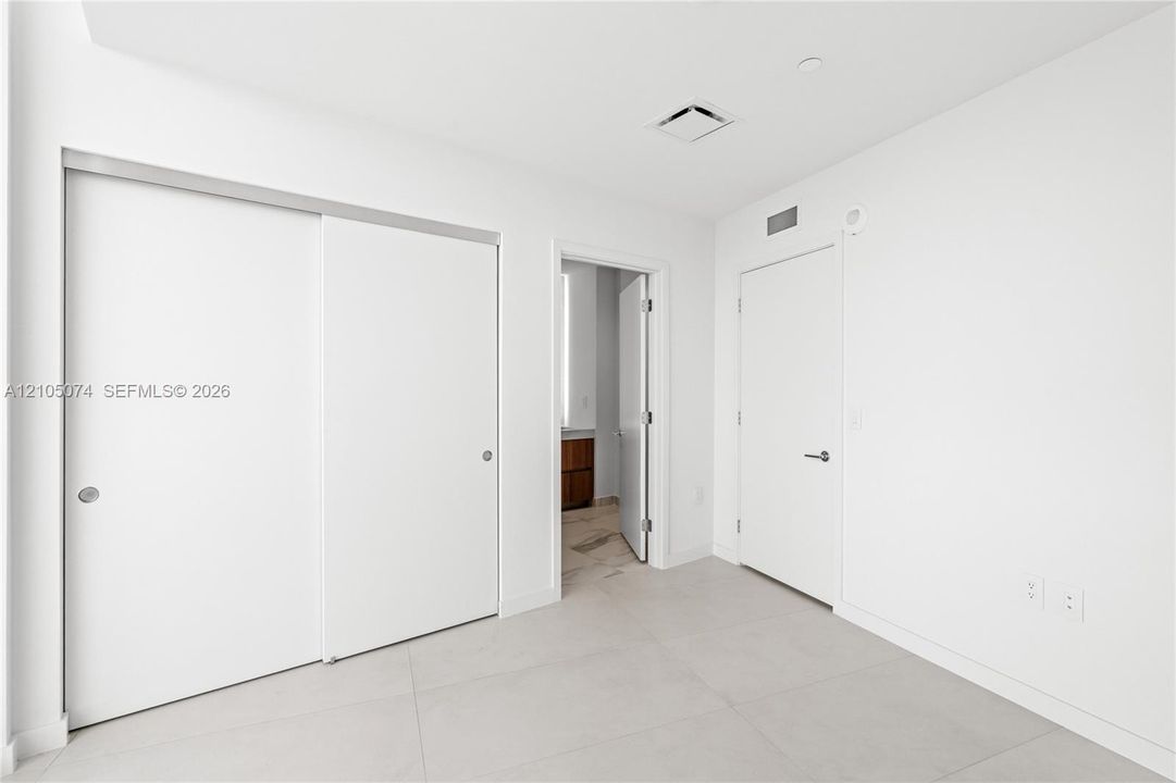 Neutral-toned large-format tile flooring, sliding closet doors, and solid-core swing door with brushed nickel hardware