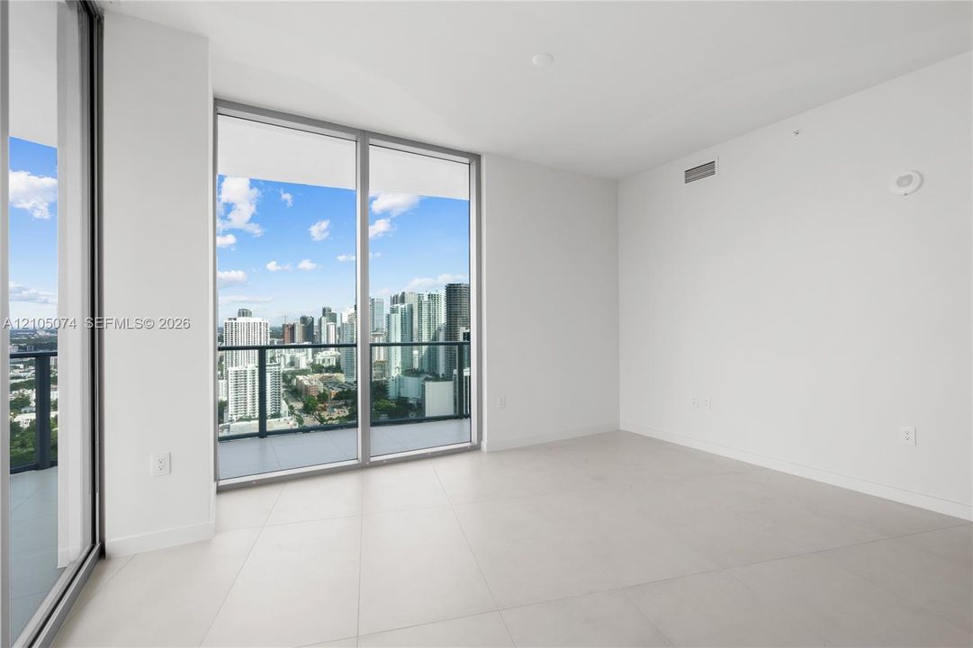 Floor-to-ceiling sliding glass doors, neutral tile flooring, and a glass-paneled balcony featuring urban skyline scenery