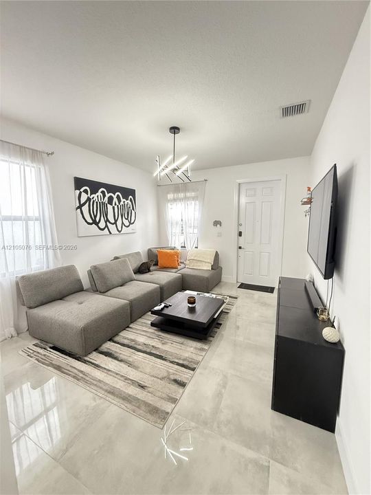Living area featuring large-format light-toned tile flooring, multi-paned windows, and a contemporary geometric chandelier