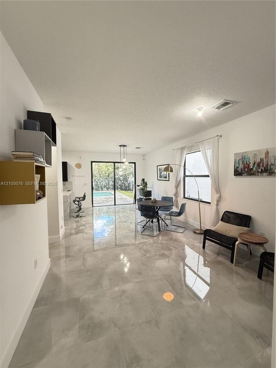 Open-concept interior featuring large-format tile flooring, recessed lighting, built-in wall shelving, and sliding glass doors revealing a swimming pool