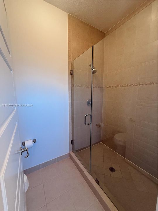 Walk-in shower enclosure with frameless glass door, neutral ceramic tile surround, integrated decorative tile inlay, and chrome finish hardware