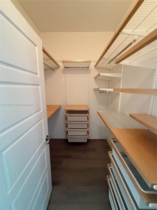 Walk-in closet featuring multi-level wood-finish shelving, integrated pull-out drawers, white metal support tracks, and dark wood-finish flooring