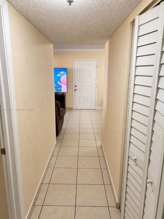 Hallway featuring neutral-toned tile flooring, white louvered-style bi-fold closet doors, and an exterior door with a multi-panel design