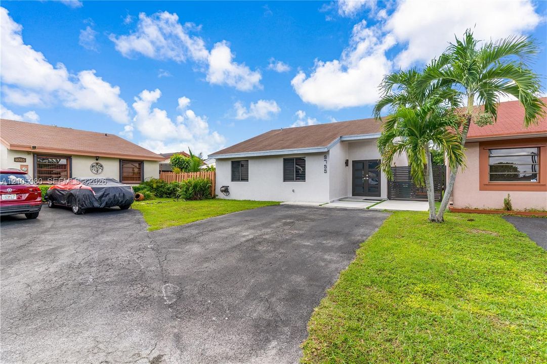 Single-story residence featuring a light-toned exterior, dark-framed double front entry doors, asphalt-paved driveway, and mature landscaping