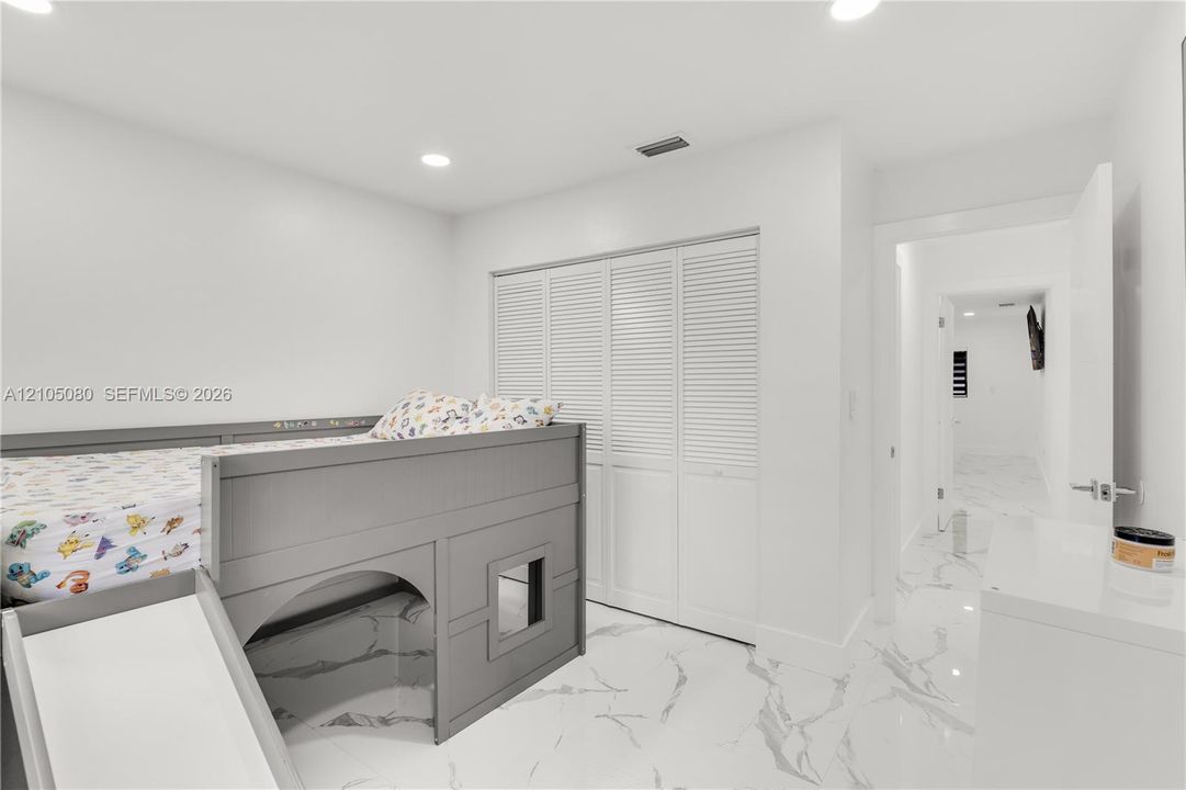 Large-format tile flooring with veined detailing, recessed ceiling lighting, and floor-to-ceiling louvered closet doors