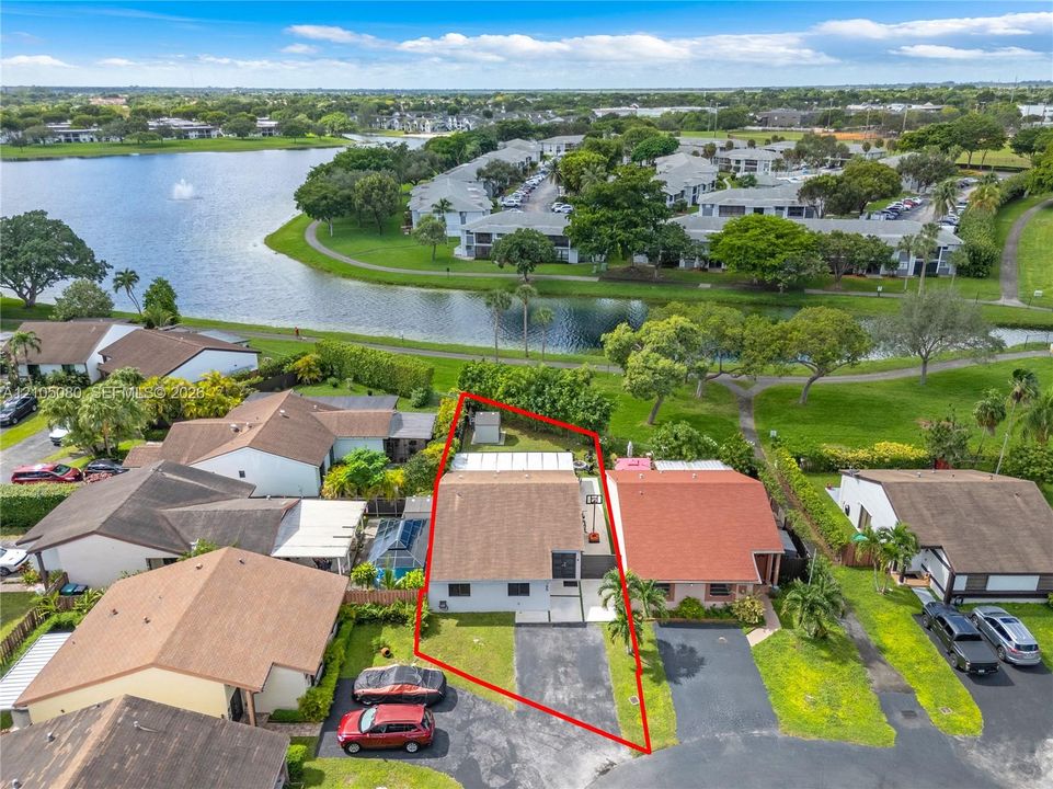 Aerial perspective featuring a single-story residence with a pitched shingle roof, paved driveway, and grass lot situated along a water feature