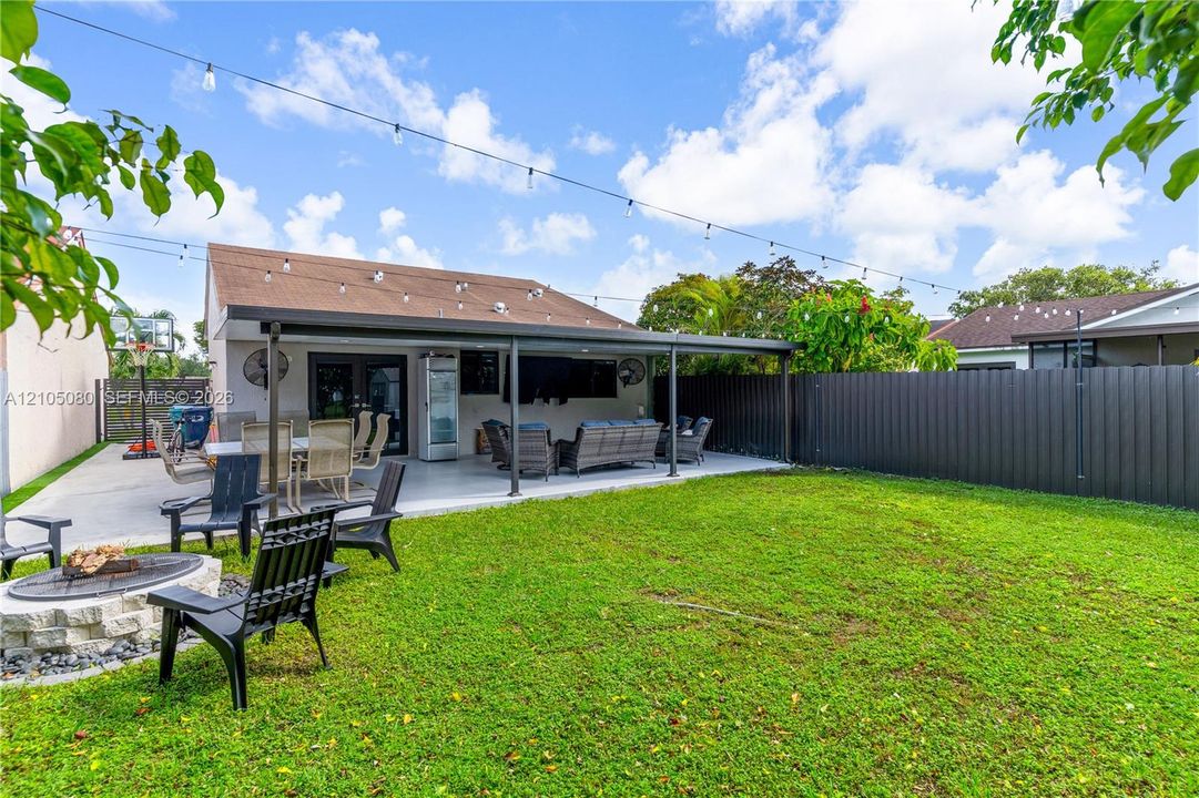 Backyard featuring a covered concrete patio, stone-finish fire pit, string lighting, and privacy fencing