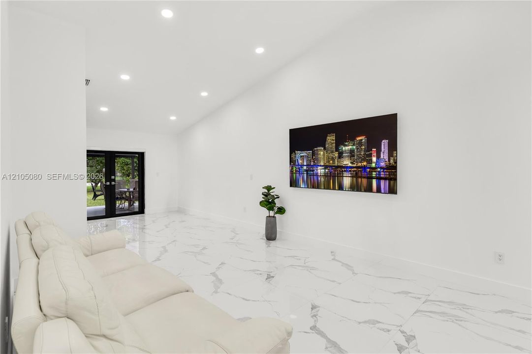 Vaulted ceiling featuring recessed lighting, large-format polished tile flooring, and black-framed French doors