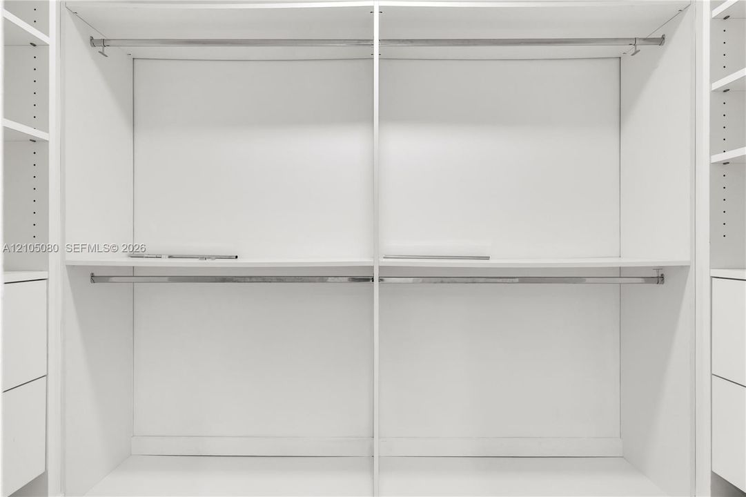 Custom built-in closet organization system featuring white cabinetry, tiered hanging rods, adjustable shelving, and integrated drawer storage