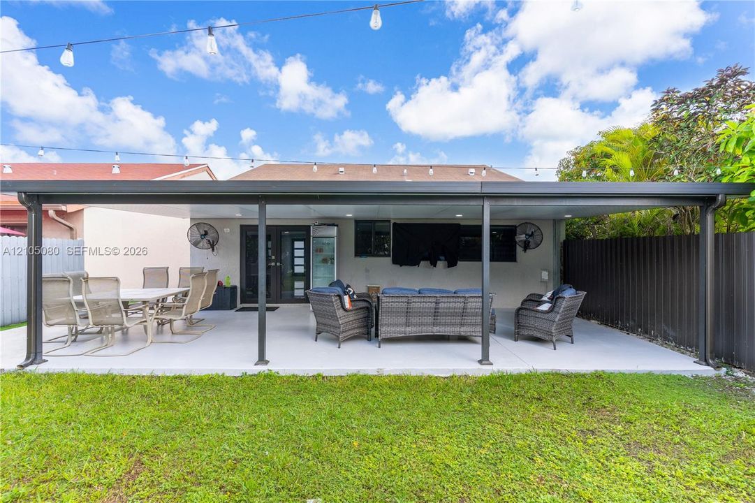 Covered patio featuring a solid roof structure, painted concrete flooring, mounted wall fans, recessed lighting, and overhead string lighting