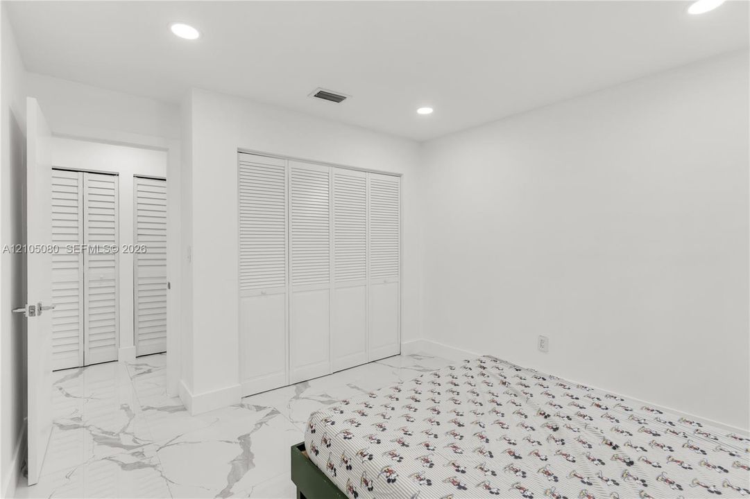Interior room featuring large-format tile flooring with a neutral veined pattern, recessed ceiling lighting, and multiple sets of white louvered-style closet doors