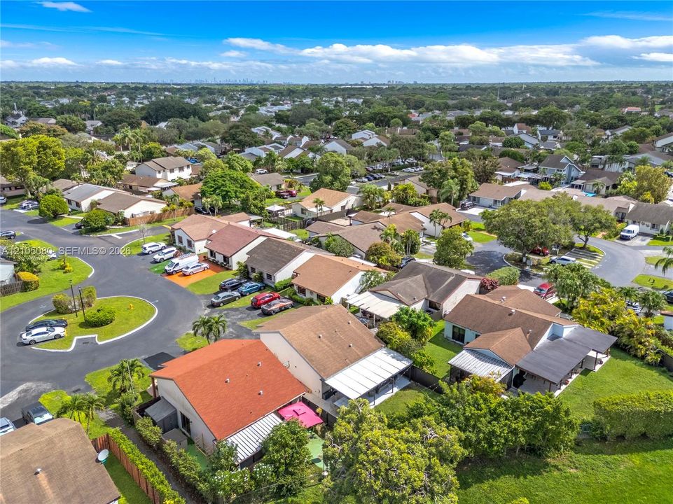 Aerial perspective of a residential neighborhood featuring paved streets, mature trees, manicured lawns, and varied single-story rooflines