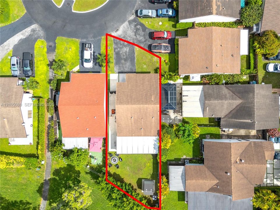 Aerial view featuring a paved driveway, shingle roof, rear concrete patio, and fenced perimeter
