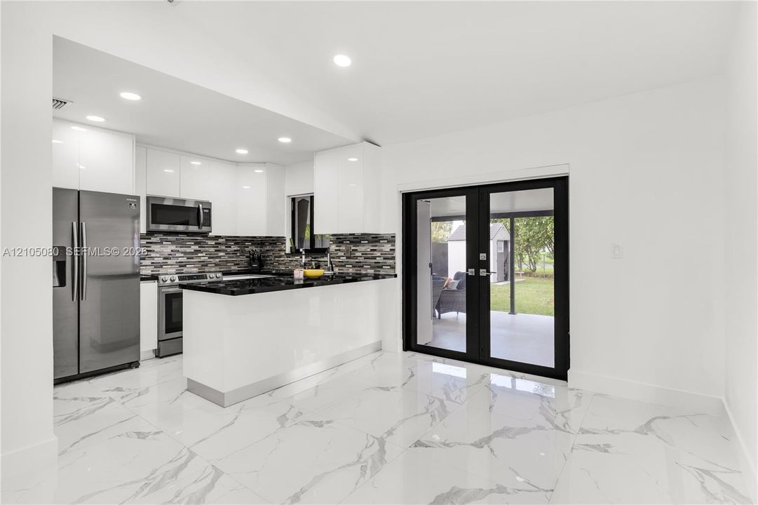 Kitchen featuring high-gloss white cabinetry, stone-finish countertops, stainless steel appliances, a multi-tonal backsplash, and large-format porcelain tile flooring with a marbled aesthetic
