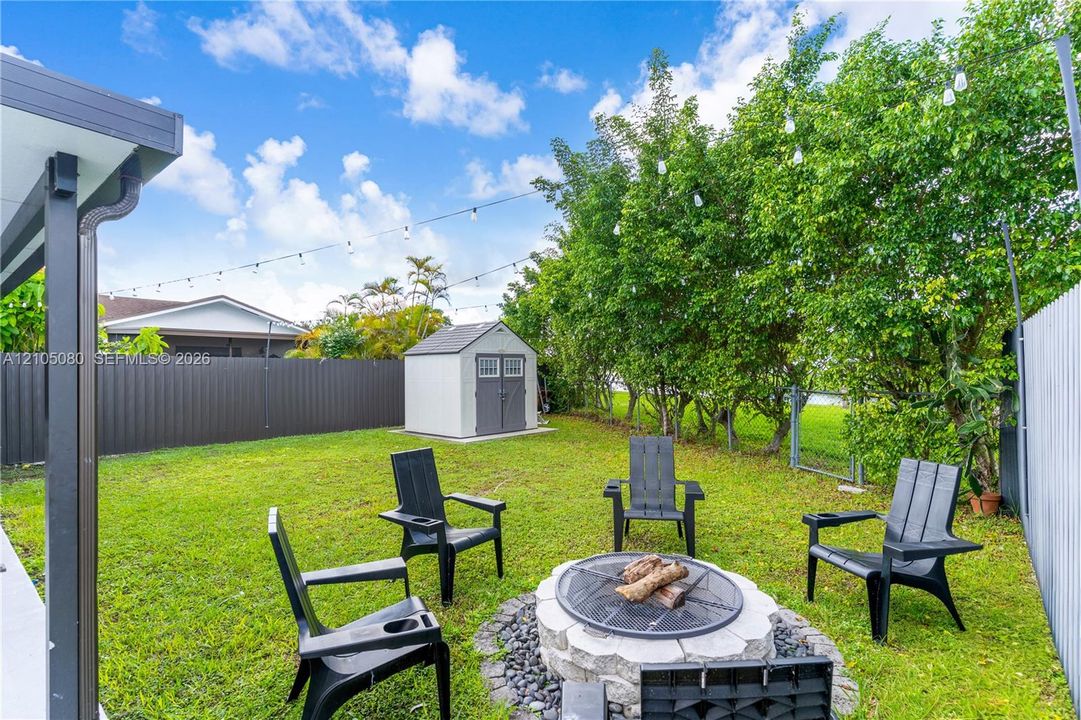 Backyard featuring a stone-encased fire pit, detached storage shed, privacy fencing, and overhead string lighting