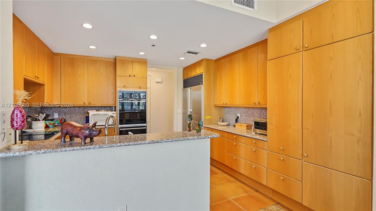 Kitchen featuring light wood-finish cabinetry, stone countertops, built-in double ovens, recessed lighting, and tile flooring