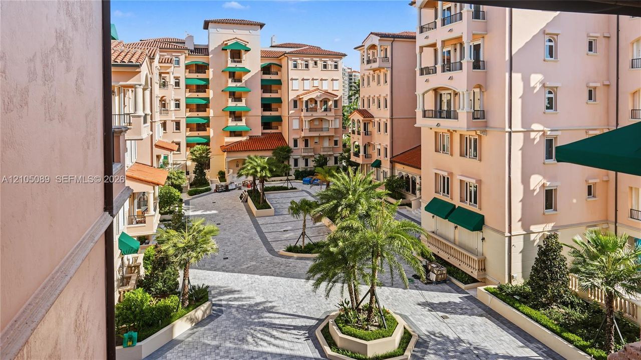 Multi-story stucco exterior featuring tile roofing, wrought iron balcony railings, arched architectural details, and a stone-paved courtyard with mature palm landscaping