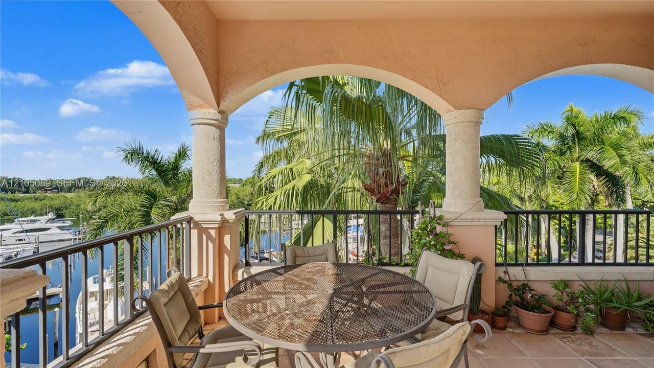 Covered terrace featuring arched masonry openings, classic columns, metal railings, and stone-tile flooring