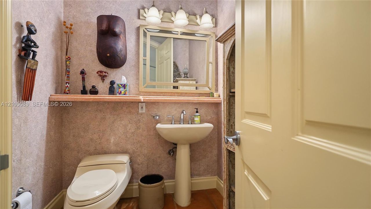 Pedestal sink with chrome faucet, stone-surfaced floating shelf, framed wall mirror, three-light fixture with glass shades, and neutral wall finish