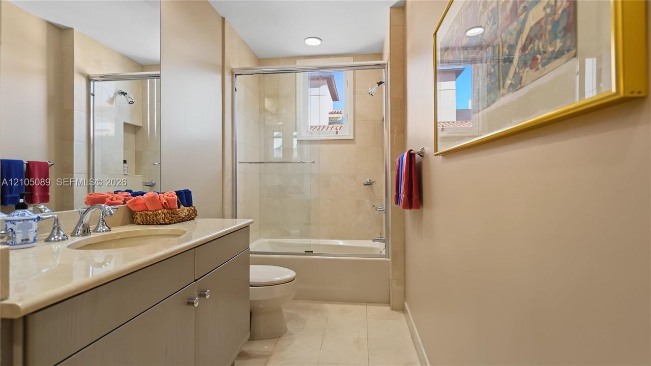 Bathroom featuring a vanity with a light-toned countertop, integrated basin, recessed lighting, and a bathtub with a glass enclosure and wall-tiled surround