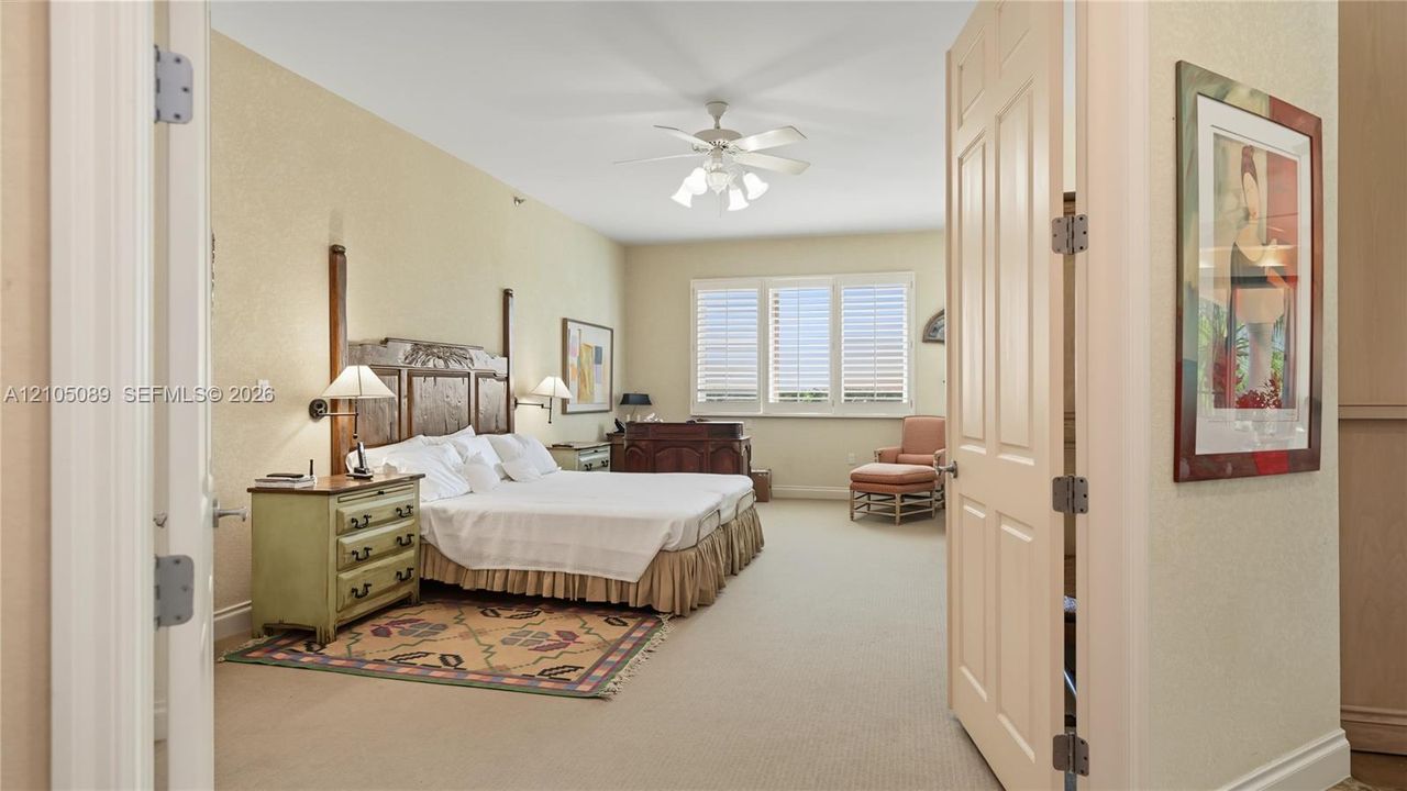 Spacious room featuring carpeting, multi-pane windows with integrated shutters, a central ceiling fan with multi-light fixture, and double-hinged doors