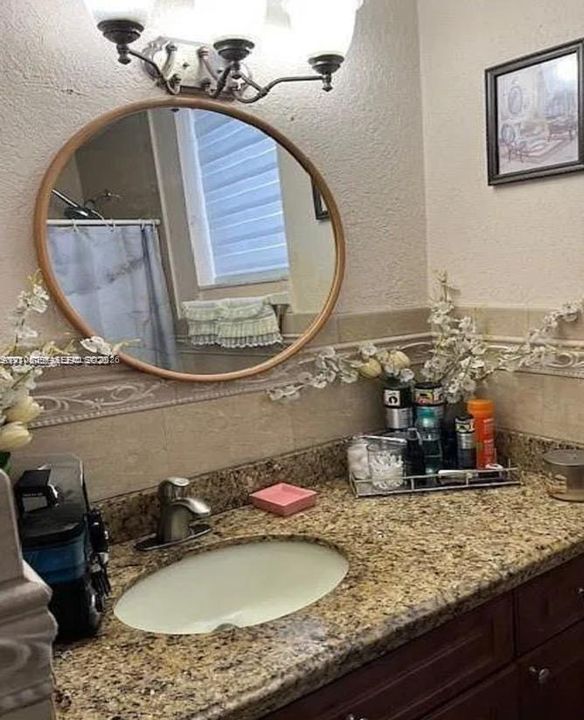 Oval vanity mirror featuring a wood-toned frame, stone-finish countertop with an integrated basin, single-handle faucet, and multi-bulb wall-mounted lighting fixture