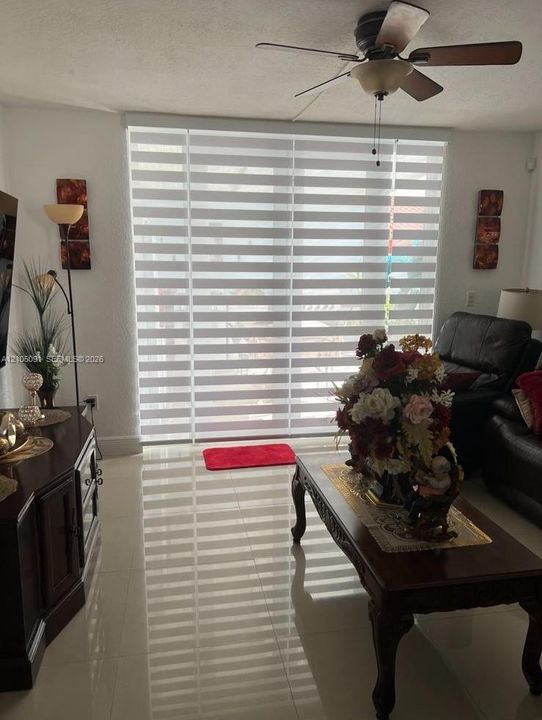 Large sliding glass door featuring adjustable horizontal blinds, light-colored tile flooring, and a ceiling-mounted light fixture with a fan