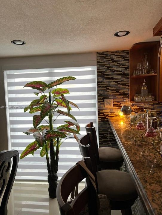 Multi-level bar area featuring a stone countertop, built-in shelving, glass-tiled backsplash, and recessed lighting