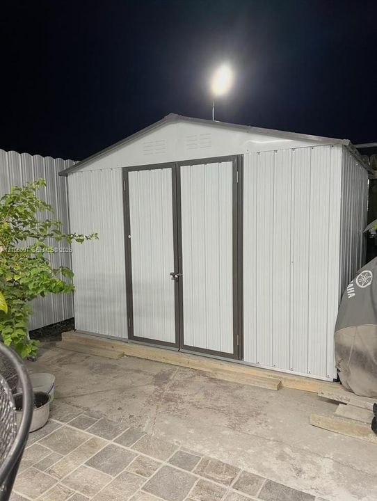 Gable-roof storage structure featuring metal panel siding, double-door entry, and a concrete foundation