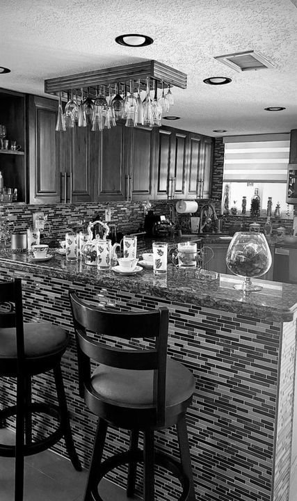 Kitchen featuring wood cabinetry, stone countertops, multi-toned linear tile backsplash, and a built-in suspended stemware rack