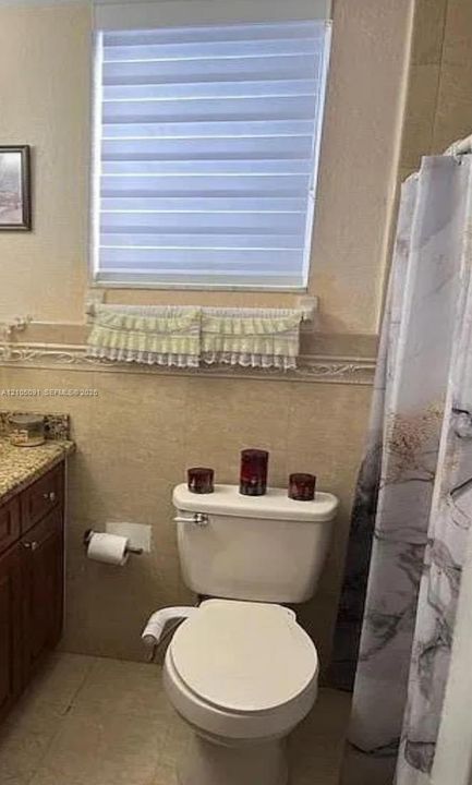 Bathroom featuring stone-finish wall tile, decorative tile molding, a single-sink vanity with stone countertop, and a window with a fitted shade