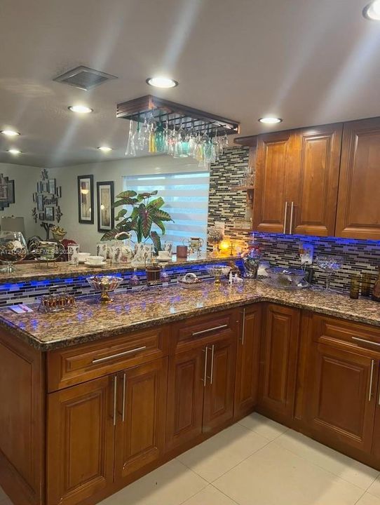 Kitchen featuring stained wood cabinetry, stone-patterned countertops, a decorative mosaic tile backsplash, and a built-in overhead glass rack