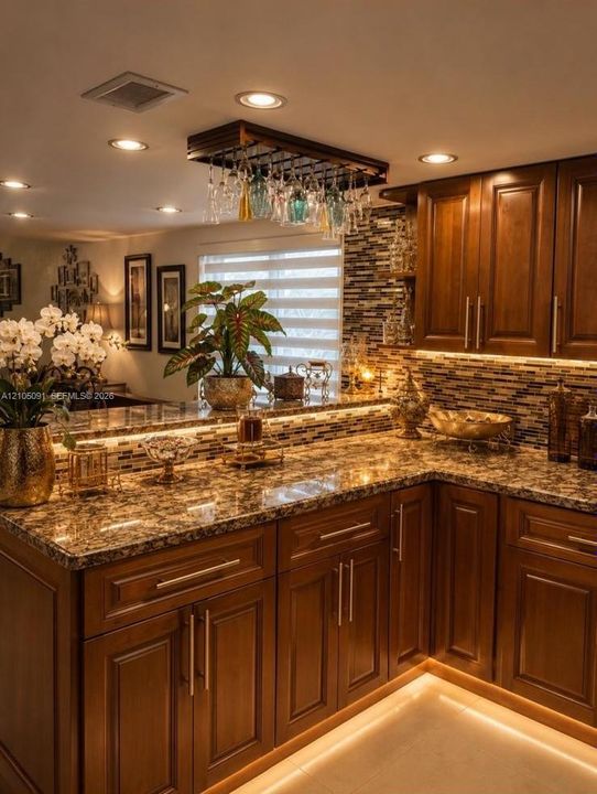Rich wood-finish cabinetry, stone-surface countertops, mosaic tile backsplash, recessed lighting, and a built-in hanging stemware rack