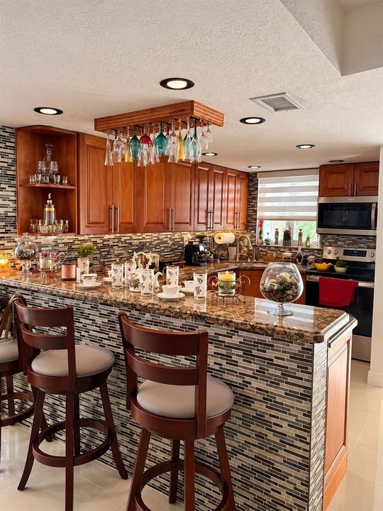 Kitchen featuring wood cabinetry, stone countertops, multi-toned mosaic tile backsplash, built-in glass rack, and recessed lighting
