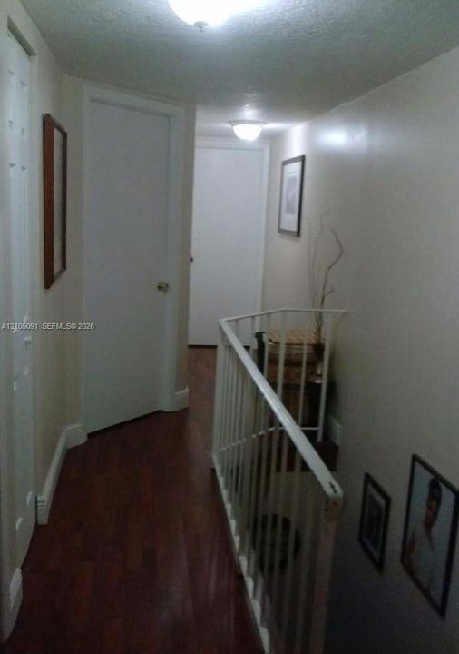 Hallway featuring wood-finish flooring, white paneled doors, and a metal stair railing