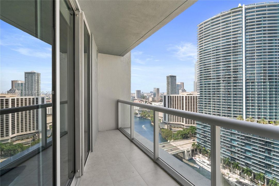 Balcony with tile flooring and a glass railing, offering urban and water scenery