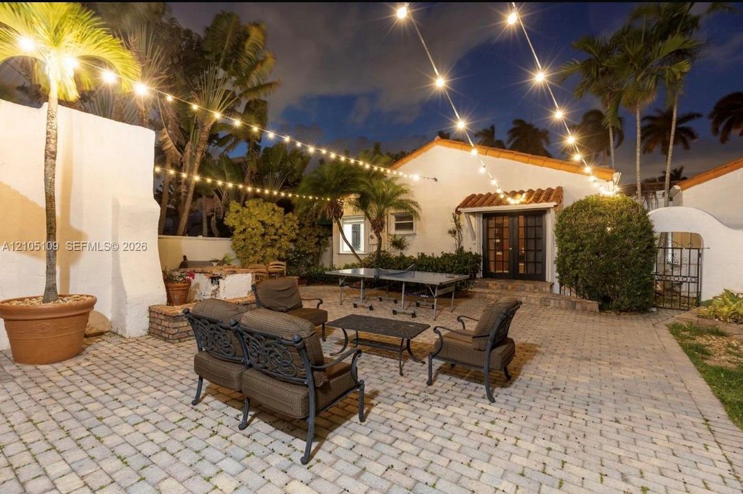 Paved patio featuring a stucco exterior, clay tile roof, and mature palm trees