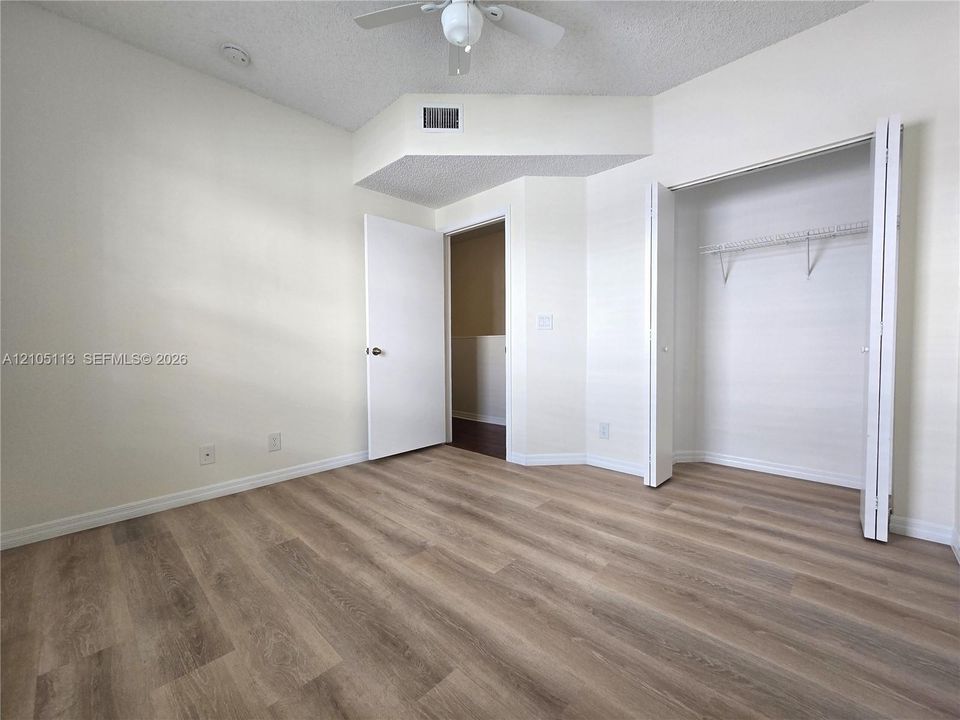 Wood-finish flooring, white walls, ceiling fan, and bi-fold closet doors with wire shelving