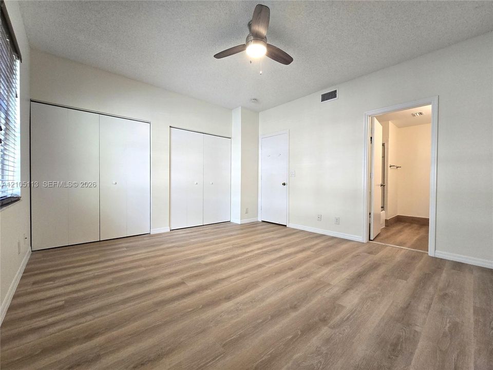 Wood-finish flooring throughout, multiple bi-fold closet doors, ceiling fan with integrated lighting, and an entryway to an adjoining room