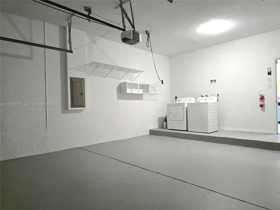 Attached garage with a utility area, overhead garage door opener, built-in shelving, and a raised platform for laundry appliances