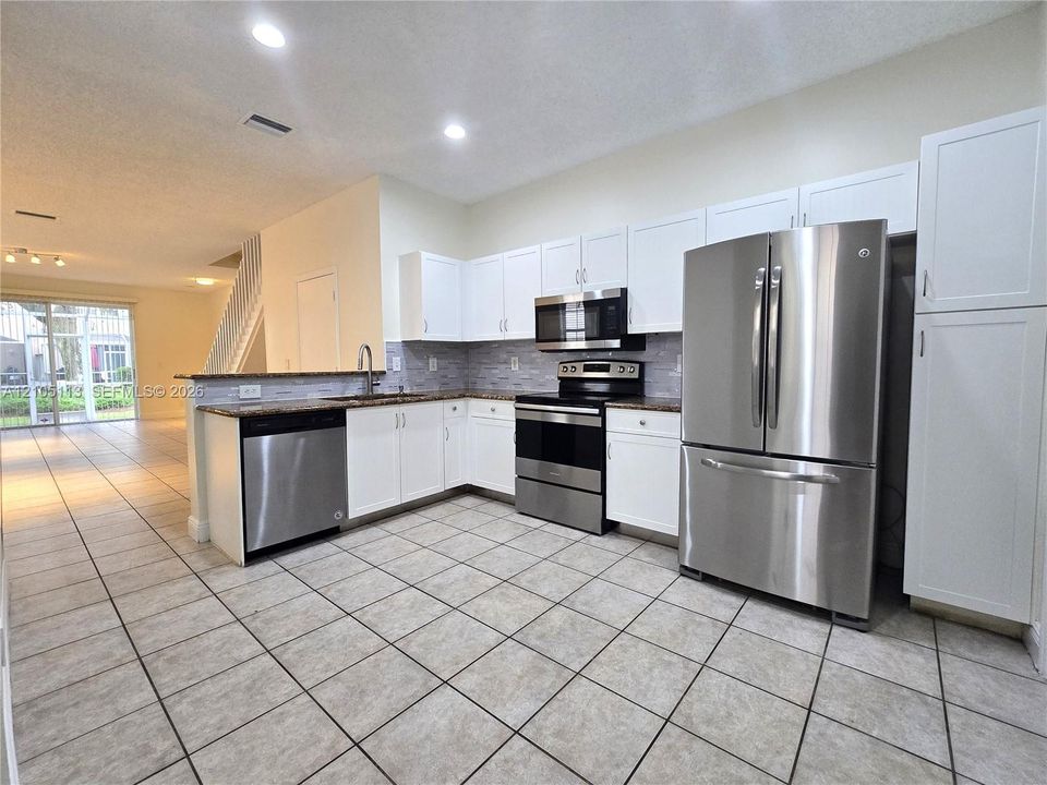 Kitchen featuring stainless steel appliances, white cabinetry, a tiled backsplash, and stone countertops