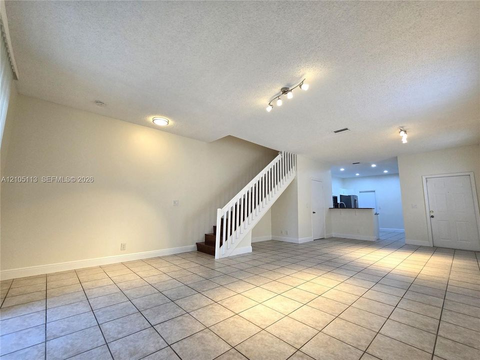 Spacious open-concept living area featuring tile flooring, a white-railed staircase with wood-finish treads, and recessed lighting