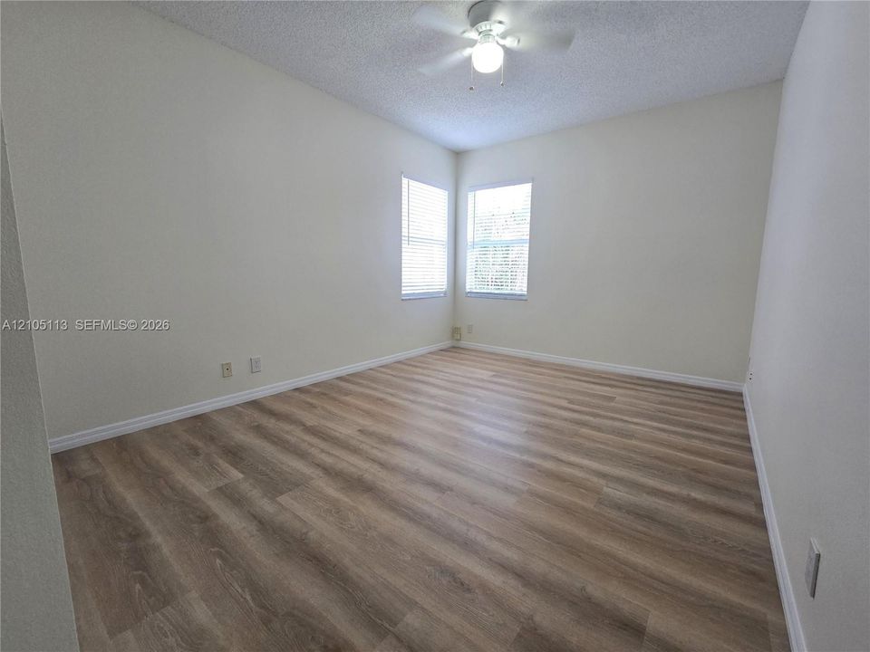 Wood-finish flooring, multiple windows with blinds, ceiling fan, and sloped ceiling