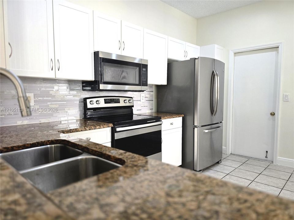 Kitchen featuring white cabinetry, stone-finish countertops, stainless steel appliances, and a mosaic tile backsplash