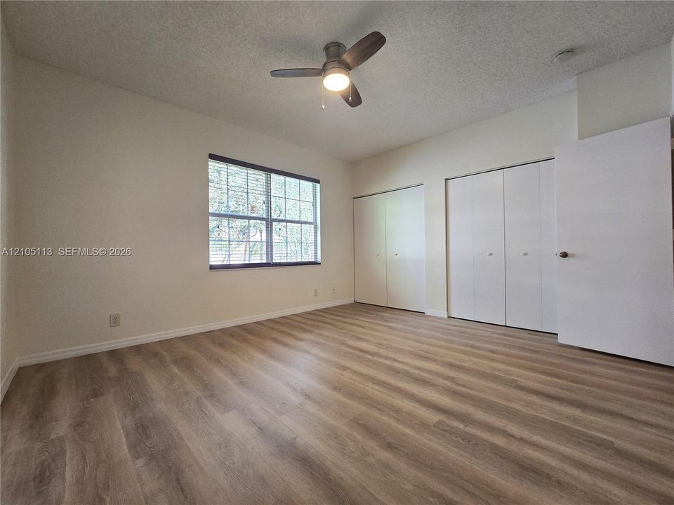 Room featuring wood-finish flooring, a ceiling fan, and multiple bi-fold closet doors