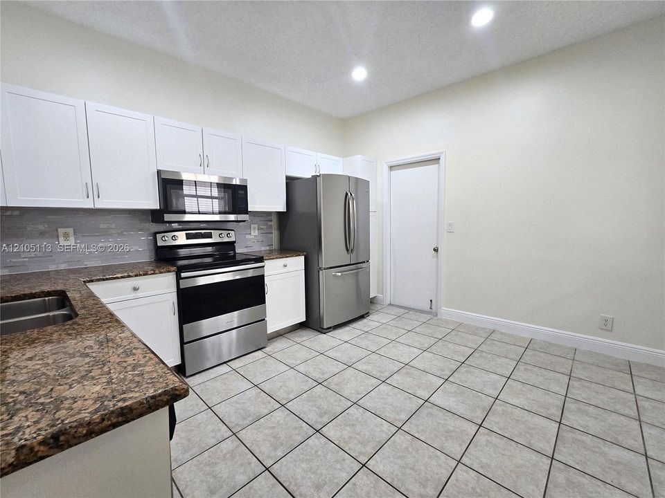 Kitchen featuring white cabinetry, stainless steel appliances, speckled countertops, a tile backsplash, and recessed lighting