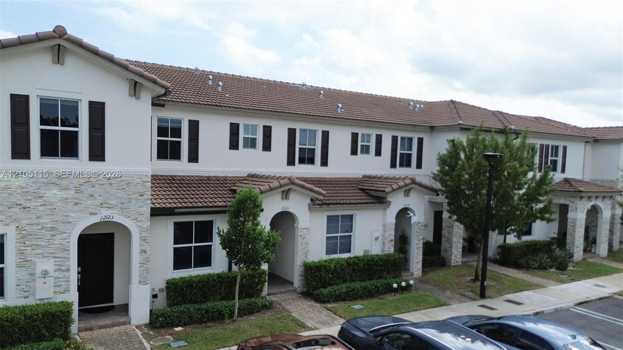 Exterior facade featuring stucco siding, stone veneer accents, multi-pane windows with decorative shutters, and tile roofing