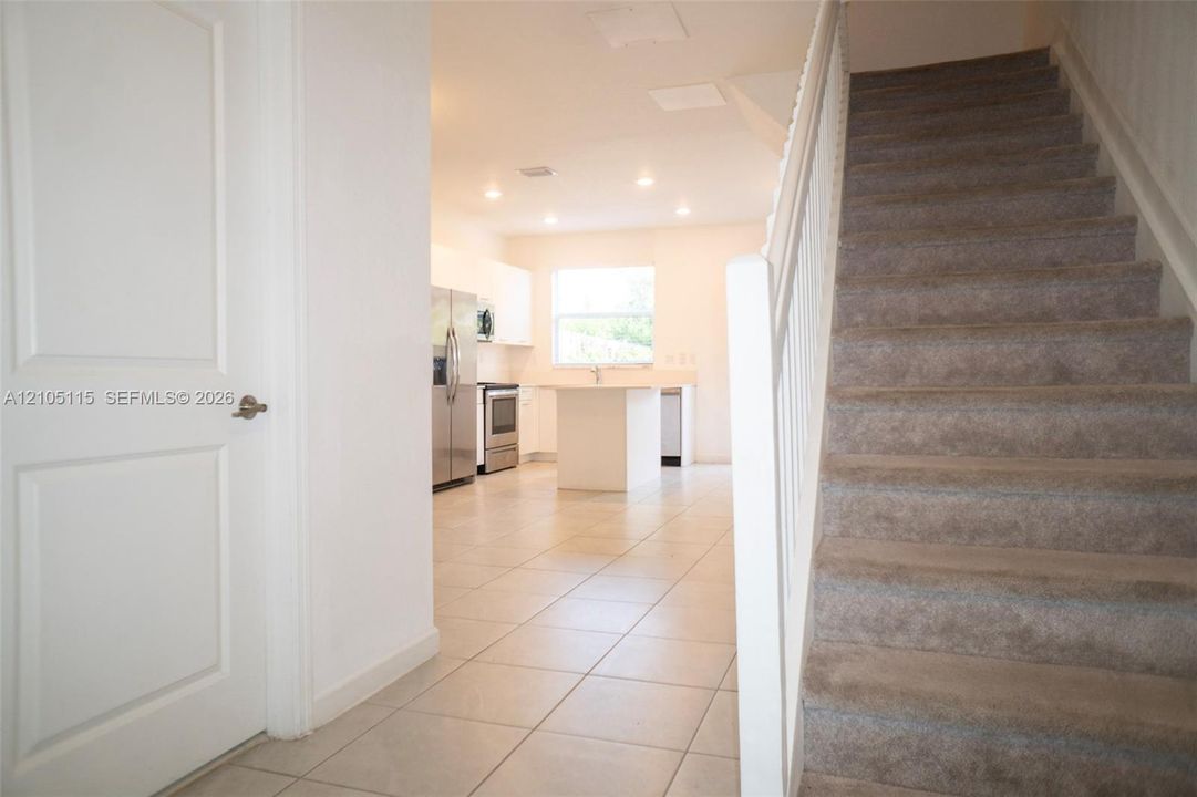 Staircase with carpeted steps and white railing, tile flooring, and kitchen featuring stainless steel appliances, white cabinetry, and central island