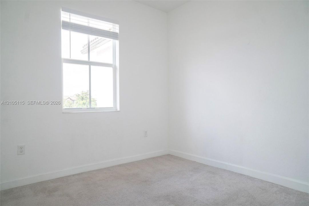 Neutral-toned carpeting, high-ceilinged room with white walls, and a single-hung window featuring horizontal blinds