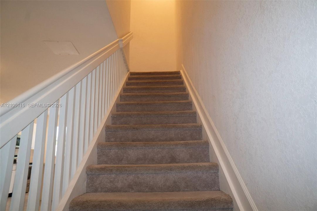 Staircase featuring wall-to-wall carpeting and a white wooden railing with vertical balusters